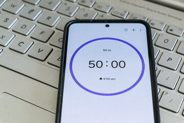 A phone with a black and white 50-minute timer to study with pomodoro method on laptop keyboard,...