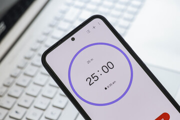 A phone with a black and white 25-minute timer to study with pomodoro method on laptop keyboard, study business background