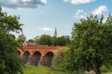 Background with an old brick bridge and a church in a small European town. Summer. Kuldiga