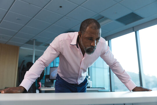 Businessman in office leaning on desk, concentrating on work in evening