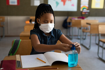 In school, young girl using hand sanitizer while studying at desk in classroom