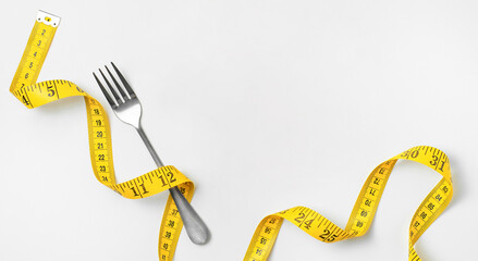 Measuring tape and fork on light background with copy space. Diet and weight loss concept