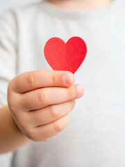 Obraz premium Child Holding a Red Heart Cutout with a Gentle Smile on a Soft Background