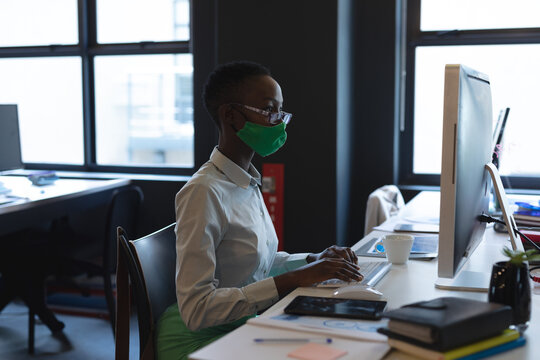 Professional woman wearing mask working on computer in modern office
