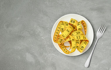 Measuring tape on white plate and fork next to it on grey background. weight loss and diet concept