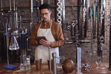 Distillery worker using tablet to monitor gin production process in factory