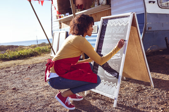 Woman updating menu on chalkboard at food truck, preparing for customers