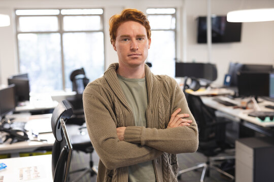 Confident man with red hair standing with arms crossed in modern office
