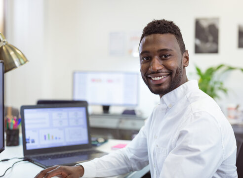 Smiling businessman working on laptop at office, analyzing data charts