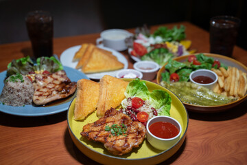 Chicken steak set with sauce, bread and salad plate on a brown wooden table in a restaurant.