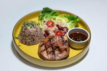 A set of pork and chicken steaks, bread and a plate of salad on a brown wooden table in a restaurant.