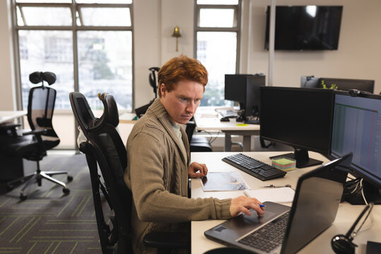 Focused man working on laptop in modern office, analyzing data on screen