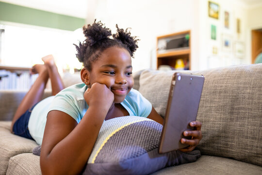 Young girl lying on couch using tablet, smiling and enjoying screen time
