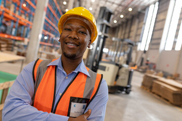 Warehouse worker in safety gear smiling confidently, standing near forklift