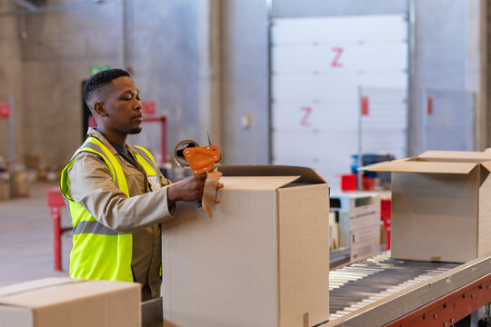 Warehouse worker sealing cardboard boxes on conveyor belt, focusing on task, copy space