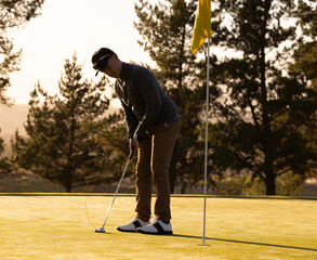 Male golfer focusing on putting ball into hole on sunny golf course