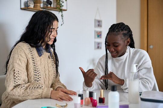 Two smiling young women painting nails at home - Powered by Adobe
