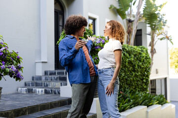 Outside modern home, diverse couple having animated conversation surrounded by greenery