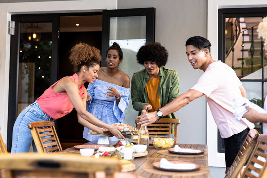 Multiracial friends enjoying on patio meal together, sharing food and laughter on sunny day