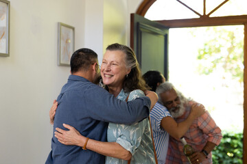 Diverse senior friends greeting friends with warm hugs at home, enjoying joyful reunion