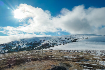 Majestic boulders frame a serene winter scene. Snow-covered Packalpe mountains stretch into the horizon under a blue sky with scattered clouds. Taken at mountain peak Seinerkreuz, Styria, Austria