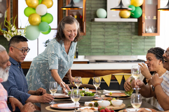 Sharing festive meal, senior diverse friends laughing and conversing together at home