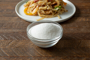 A view of a small bowl of MSG, next to a noodle entree.
