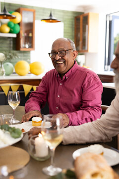 Celebrating birthday, senior man holding cupcake with diverse friends at home