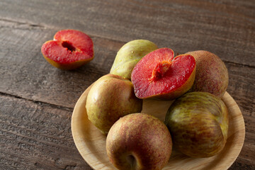 A view of a plate of speckled plumcots, featuring one that is cut in half, revealing its pit.