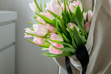Pink tulips bouquet in hanged on the door shopper bag at home close up