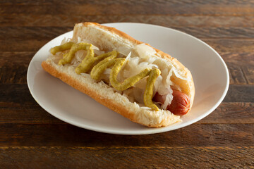 A view of a hot dog with sauerkraut and brown mustard.