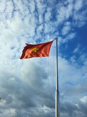 A Vietnamese national flag waves majestically against a bright blue sky with scattered white clouds.