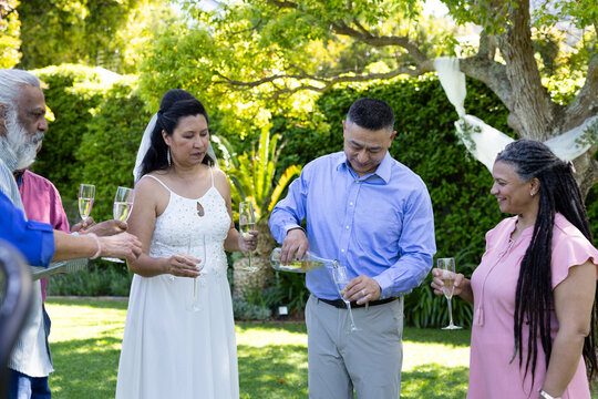Celebrating in garden, senior diverse friends pouring champagne at wedding reception