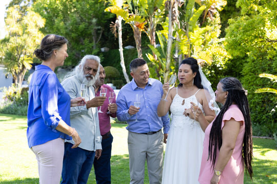 Celebrating in garden, diverse seniors with champagne engaging in lively wedding conversation