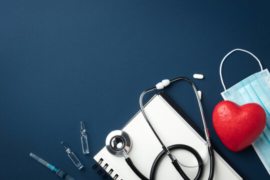 Red heart with doctor stethoscope, medical instruments and notebook on blue background, hospital life insurance concept, world heart health day. Copy space.