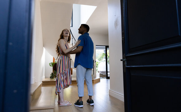 Young diverse couple smiling and embracing in modern home entrance hallway - Powered by Adobe