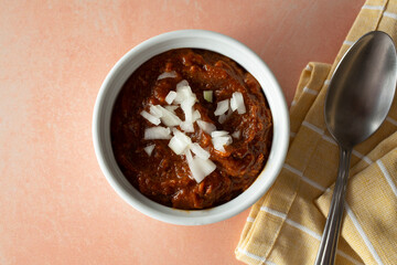 A top down view of a bowl of chili, topped with chopped onions.