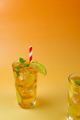 One glass of a ice tea with lime and lemon slices in it. The drink is served in a glass with mint leaves on the top and white and red straw. Another glass of ice tea in the bottom right corner. Warm o
