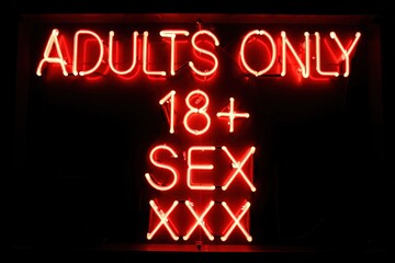 Obraz premium Bright neon sign indicating adults only with emphasis on 18 plus age restriction and sexual content in a nightlife setting