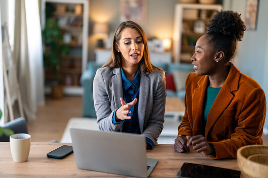 Two Diverse Business Women Having Productive Discussion At Home Office Desk With Laptop And Coffee