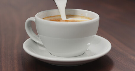 pour steamed milk into cappuccino white cup on walnut table