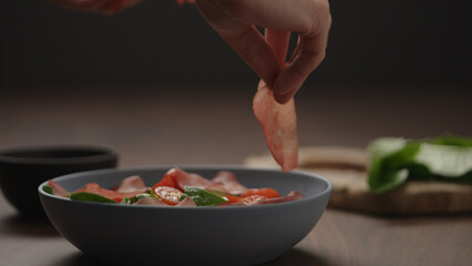 man add bresaola to salad in blue bowl