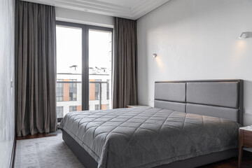 modern bedroom interior in stylish apartment. large double bed in grey with clean linens and grey bedspread. stylish wooden bedside table next to bed. Photograph of bedroom with different lighting