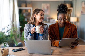 Two Professional Women Collaborate in Bright Home Office Setting with Modern Devices