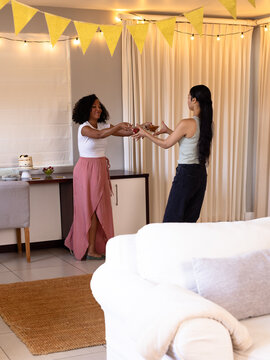 Two diverse female friends exchanging gifts at home, celebrating with joy and laughter