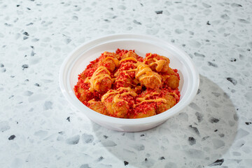A view of a container of tater tots topped with spicy chip crumbles and nacho cheese.