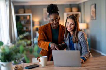 Diverse Female Entrepreneurs Collaborating with Laptop in Cozy Home Office Setting