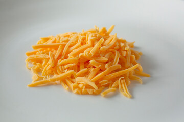A view of a pile of shredded cheddar cheese, on a white plate.