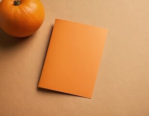 An orange card resting beside a fresh orange on a beige surface.