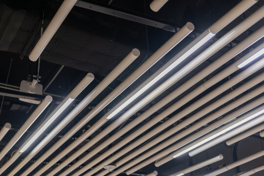 Suspended tube ceiling decoration with integrated linear lighting for diffused illumination, ideal for public space - Powered by Adobe